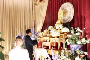 พิธีบำเพ็ญกุศลถวายเป็นพระราชกุศล: ผู้ชายจุดธูปหน้าแท่นบูชาตกแต่งดอกไม้ สวพ. มร.เพชรบูรณ์